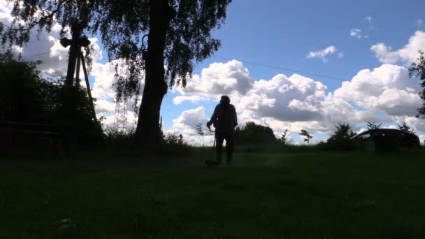 Silueta de la hierba cortada trabajador con trimmer en la tarde temprano — Vídeos de Stock