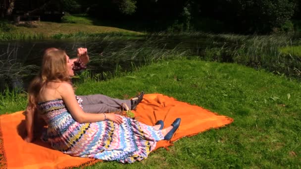 Paar isst Weintraube auf Plaid in der Nähe des Baches. Picknick im Sommer — Stockvideo