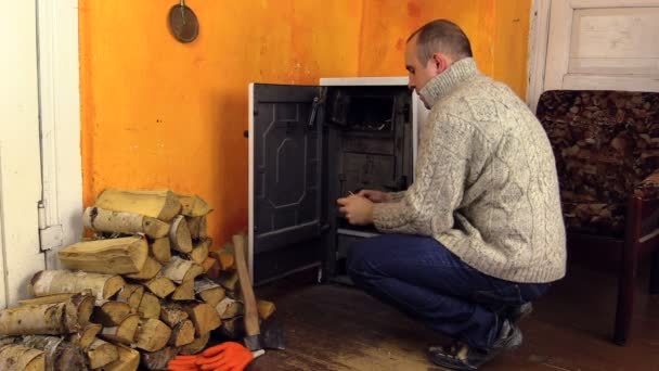 Dorpsbewoner man in de trui licht brandhout in fornuis met wedstrijd — Stockvideo