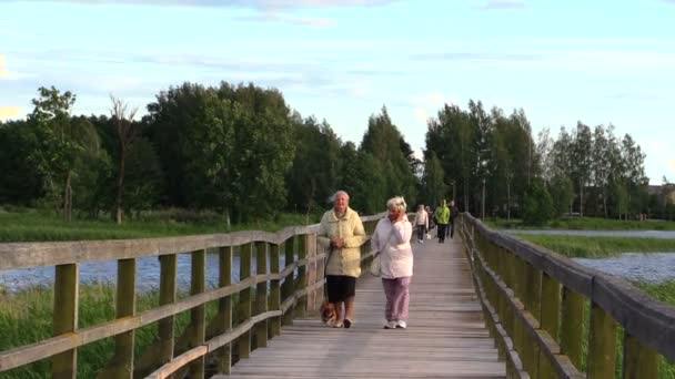 Люди йдуть давно дерев'яний міст через озеро, вечірнє небо слабкому вітрі — стокове відео