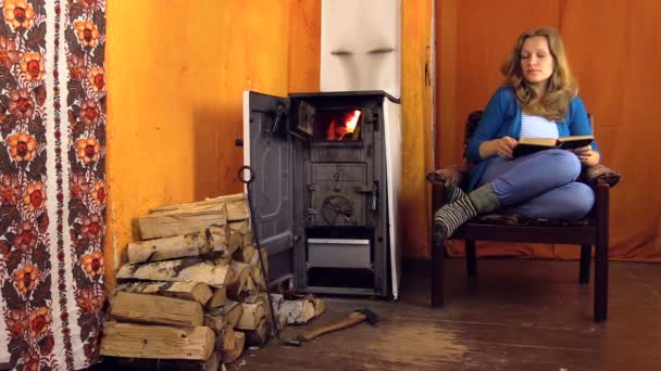 Woman sit on armchair at home, read book near stove — Stock Video