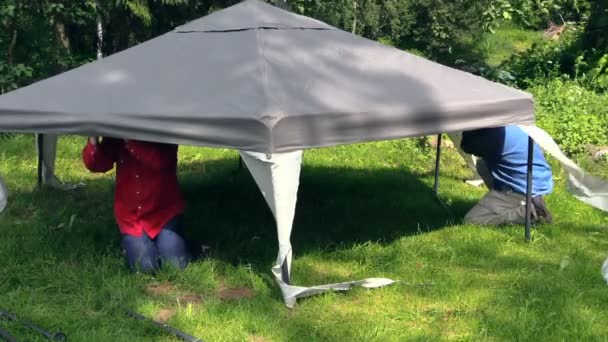 Män kröp under lusthus canvas övre fix på metall struktur — Stockvideo