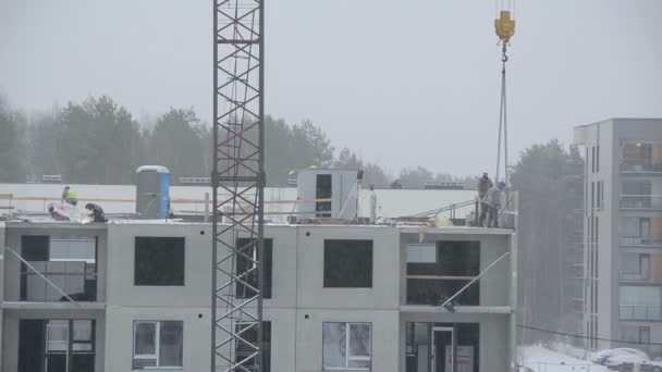 Trabajadores del sitio de construcción construyen casa. Nieve cayendo — Vídeo de stock