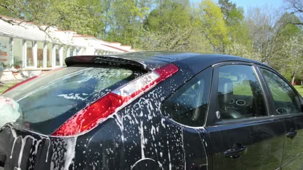 Close-up van de mens wassen zwarte favoriete auto met schuim en spons — Stockvideo