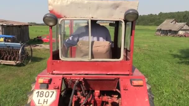 Bonden kör en gammal röd traktor genom äng — Stockvideo