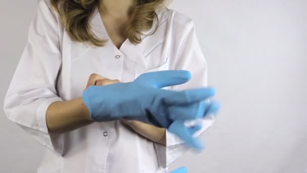 Frau im weißen Kittel zieht blaue Gummihandschuhe an — Stockvideo
