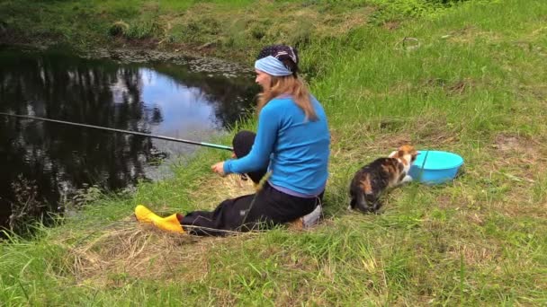 Niedliche gestromte Katze fängt Fische aus Eimer und trächtiges Mädchen angelt — Stockvideo