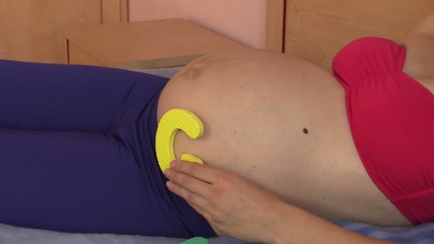 Беременная женщина выбирает слово девушка из букв игрушки на животе — стоковое видео