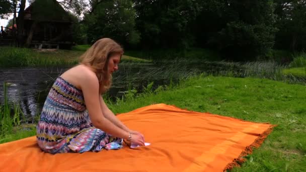 Gravid kvinna sitta på Pläd nära floden bevattnar och flex papper fartyg — Stockvideo