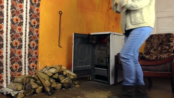 キャップを持つ女性の木材を運ぶし、燃えるストーブの近くに置く — ストック動画