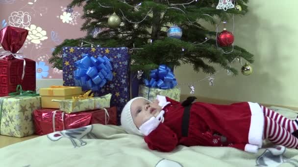 Mooie babymeisje liggen in de buurt van de kerstboom en huidige geschenkverpakkingen — Stockvideo