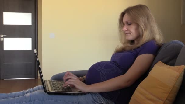 Pregnant woman working online with laptop lying on sofa at home — Stock Video