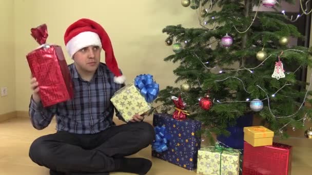 Hombre cheque sacudida regalo cajas cerca del árbol de Navidad — Vídeo de stock