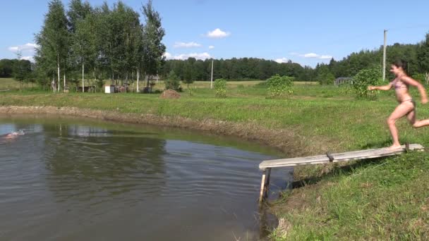 Dziewczyna i człowiek z kapelusz skok w staw z kładką. Zabawy na zewnątrz — Wideo stockowe