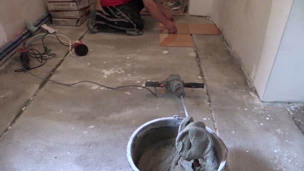 Відро з цементного клею і людини вимірюють плитку на підлозі — стокове відео