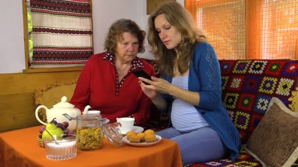 Niña y la abuela se sientan en la mesa con té, ver la foto en el teléfono — Vídeos de Stock