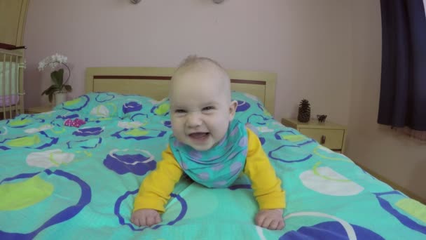 Весела новонароджена дитина посміхається і сміється лежати на животі на ліжку. 4-кілометровий — стокове відео