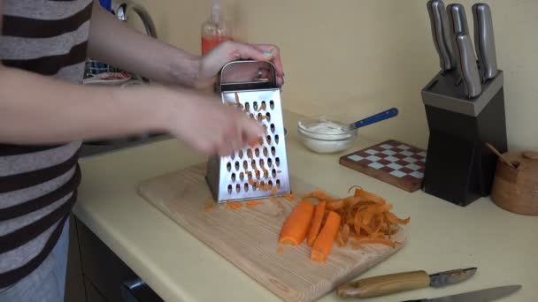 Donna mano grattugia carota arancione con strumento trituratore in cucina. 4K — Video Stock