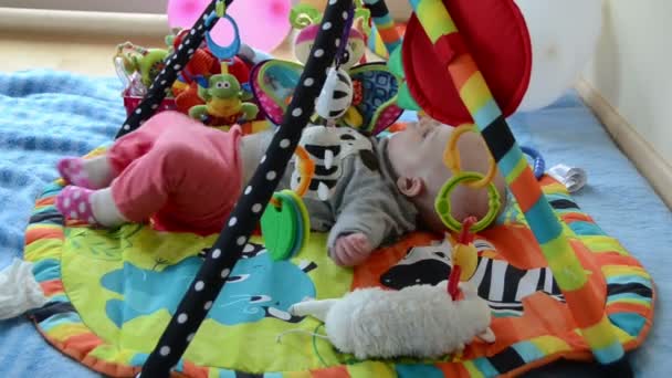 Новонароджена мила дитина грає між іграшками на барвистому маті розвитку — стокове відео