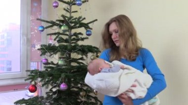 Gülümseyen anne sway yeni doğan bebek Noel ağacı yakınındaki elinde