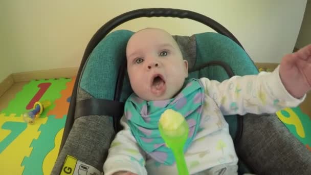 手は、緑のスプーンでよだれかけお粥と腹を空かした赤ちゃんをフィードしました。4 k — ストック動画