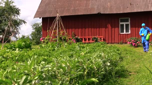 Rolnik człowiek w niebieskim wodoszczelną chodzić z zraszaczy narzędzie — Wideo stockowe