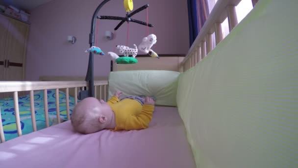 Bebê na cama de madeira tentar pegar brinquedo carrossel. 4K — Vídeo de Stock