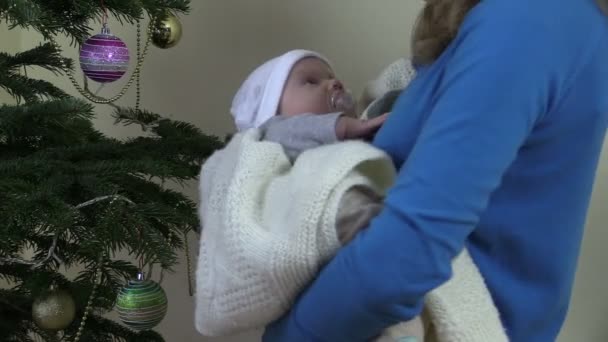 Closeup of mother cradle baby in hands near Christmas tree — Stock Video