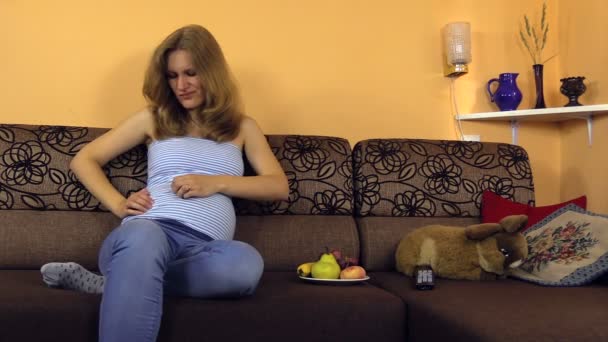 Gravid kvinna sitta på soffan och reglera speciella byxor rem — Stockvideo