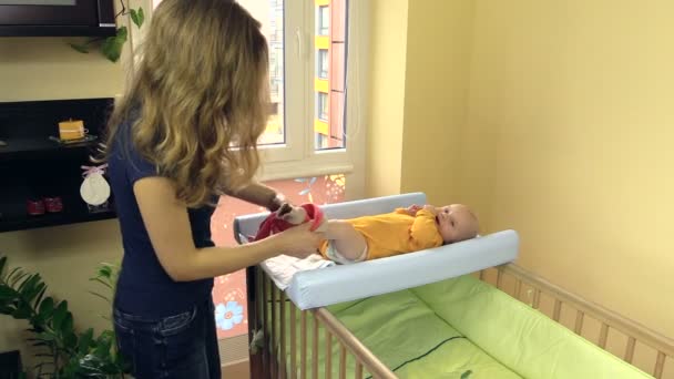 Mãe vestir bebê com calças rosa. O miúdo deita-se na mesa — Vídeo de Stock