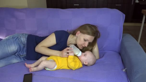 Moeder en baby liggen op Bank, feed melk fles. Kind zorg moederschap — Stockvideo