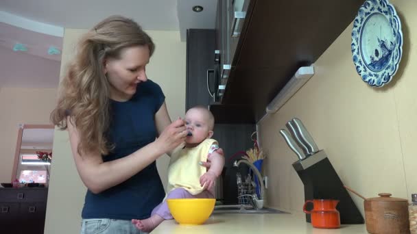 Mulher babá descuidada alimenta bebê na mesa na cozinha. 4K — Vídeo de Stock