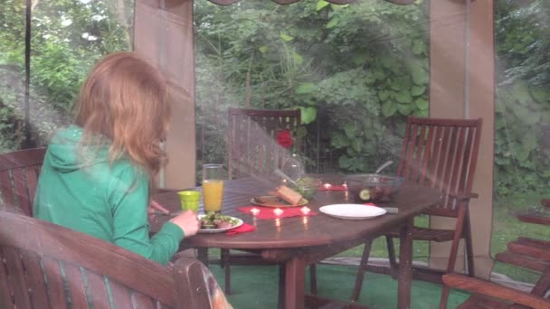 Chica comer carne solo en gazebo. Mesa de cena con vela, flor — Vídeos de Stock