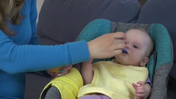 Pretty ung kvinna feeds dotter baby med sked hemma. 4K — Stockvideo