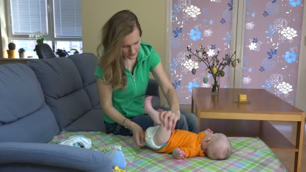 Donna vestire la bambina con un panno del corpo di colore arancione sul divano. 4K — Video Stock