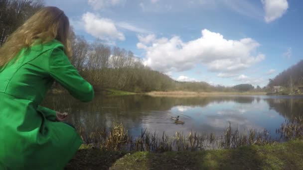 Blond tjej med gröna rocken utfodring anka fåglar nära lake. 4k — Stockvideo