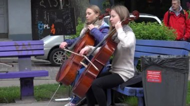 Öğrenci kızlar viyolonsel araç park bankında üzerinde oynamak. 4k