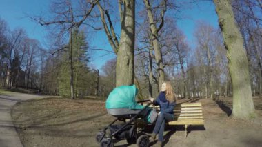 Mutlu anne bebek arabası ile bahar parkta bankta oturmak. 4k