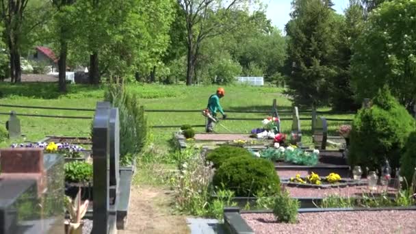 Man med trimmern gräs nära kyrkogården monument. 4k — Stockvideo