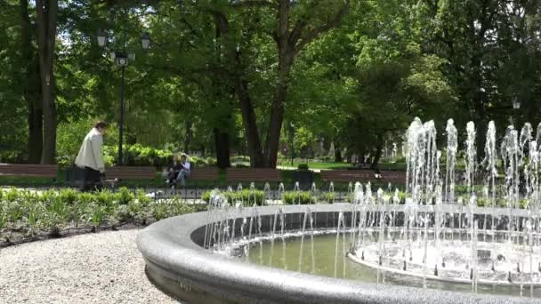 A água da fonte moderna aumenta e as pessoas recriam no parque. 4K — Vídeo de Stock