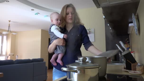 Nanny with baby in hands cooking mix meal in pot and taste. 4K — Stock Video