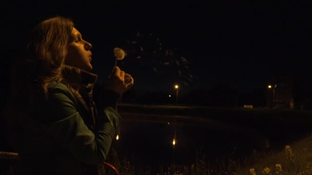 Menina sopro desflorada dente-de-leão semear sementes de flores de cardo à noite. 4K — Vídeo de Stock