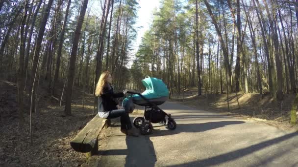 Мама сидит на скамейке с коляской. Материнство, детская концепция. 4K — стоковое видео