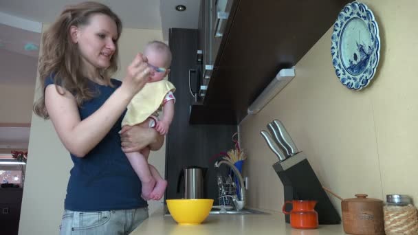 Woman hold her baby daughter and feed with spoon in kitchen. 4K — Stock Video