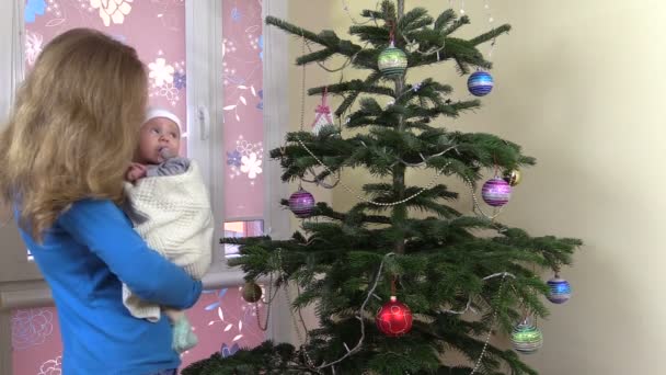 Madre bacio bambino carino e ondeggiare nelle mani vicino all'albero di Natale — Video Stock