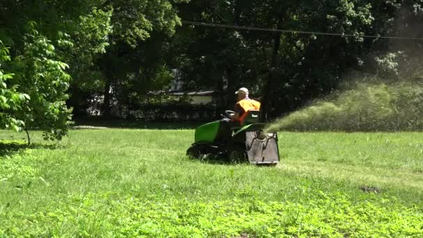 Садовник в оранжевом жилете на тракторе стрижет газон. 4K — стоковое видео