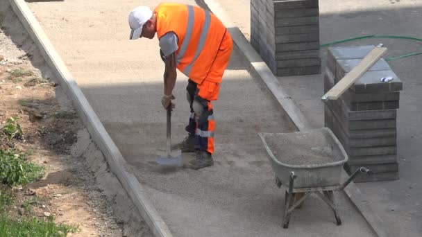 Werknemer niveau zand op nieuwe bestrating en lading in barrow. 4k — Stockvideo
