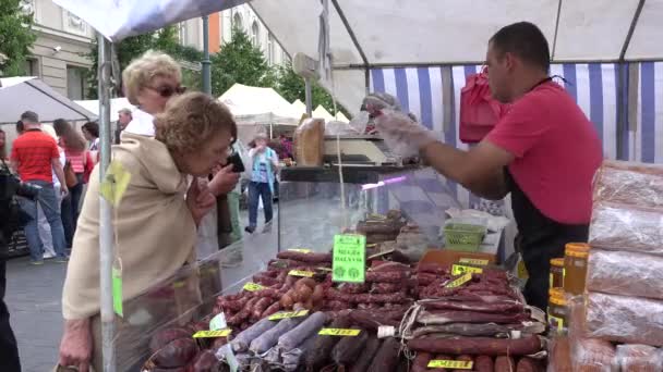 Carniceiro vendedor homem vender carne defumada para a mulher mais velha no mercado da cidade. 4K — Vídeo de Stock
