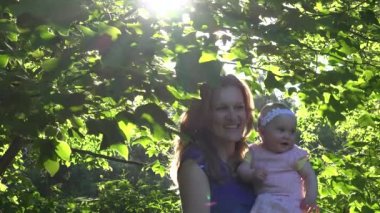 Genç neşeli anne bebek kızı Lale ağacı dalları arasında yürümek. 4k