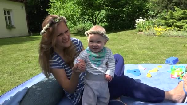 Mère aimante et bébé en couronne de fleurs couronnes dans le jardin. 4K — Video